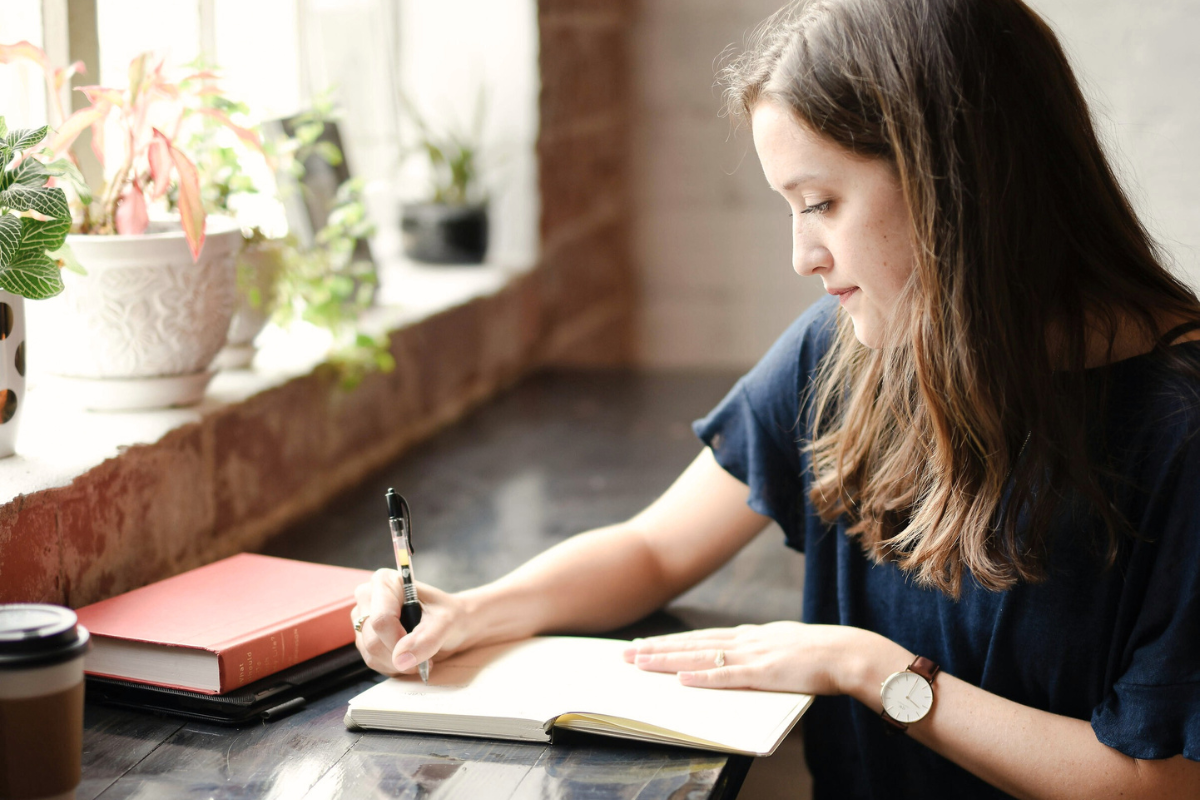 female student writing in book in cafe